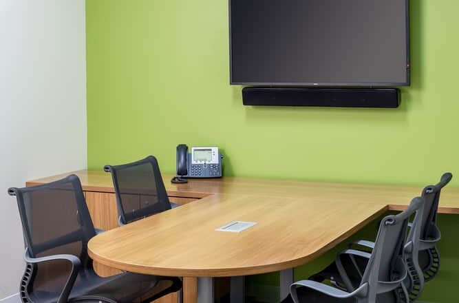 An MPCA collaboration space with a TV monitor, windows to the outer office, and a green colored accent wall.