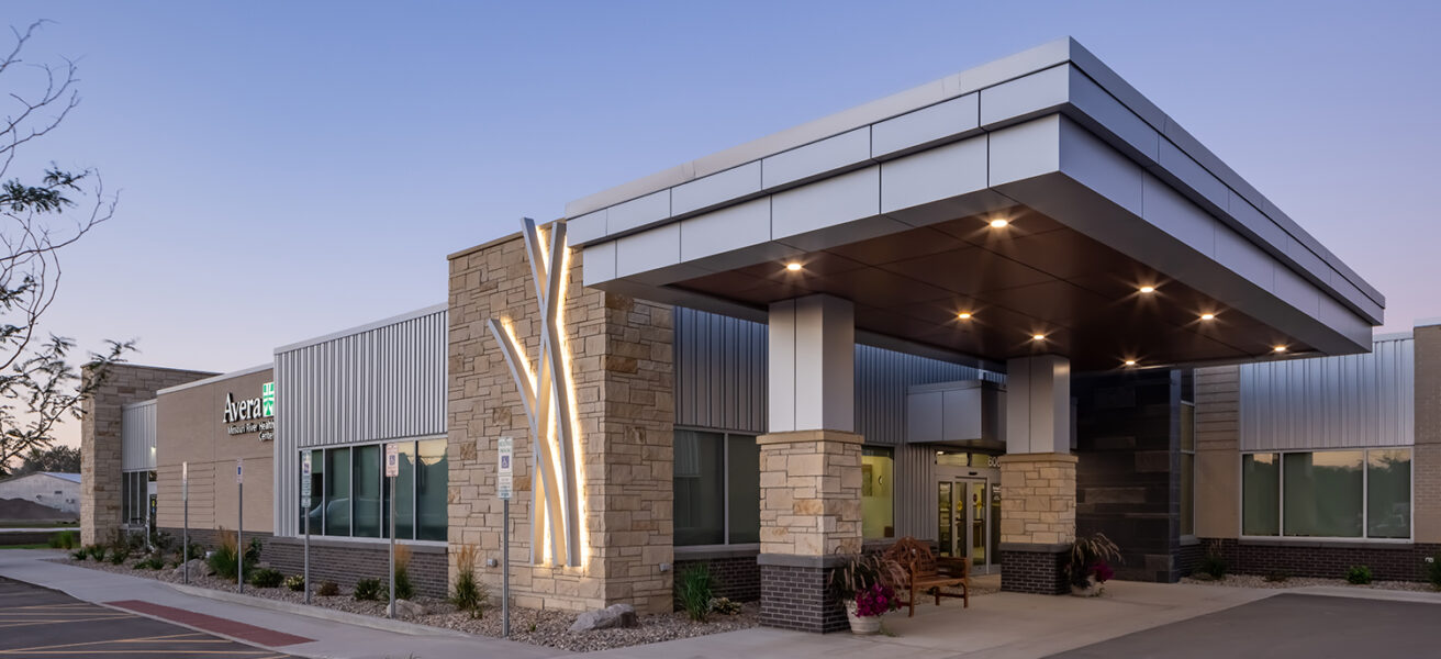 Exterior view of an Avera Missouri River entry at dusk with lighted prairie grass designs.