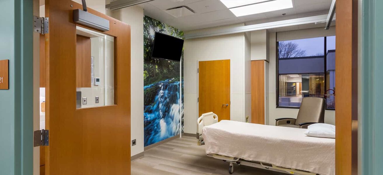 A burn unit patient room with waterfall wall mural and view to the outdoors.