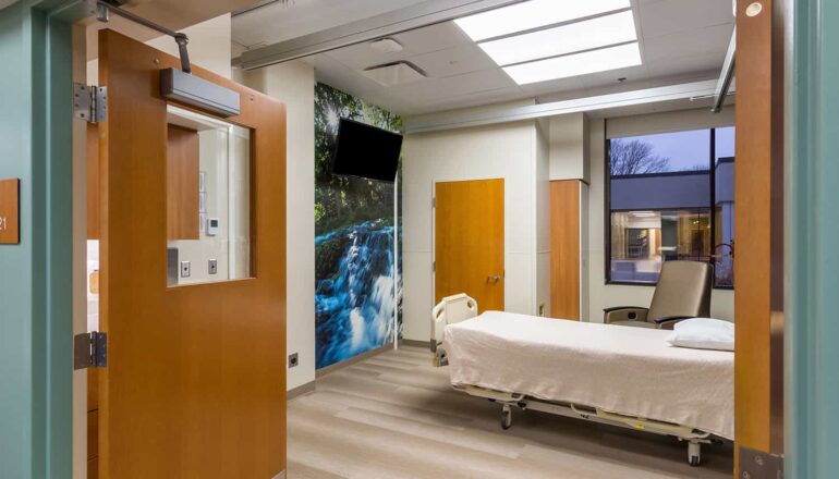 A burn unit patient room with waterfall wall mural and view to the outdoors.