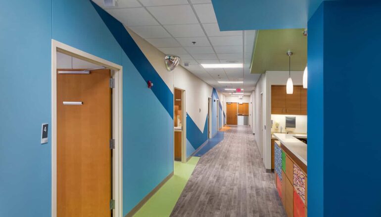 Pediatric unit corridor with a blue wall theme and view to the nurses station.