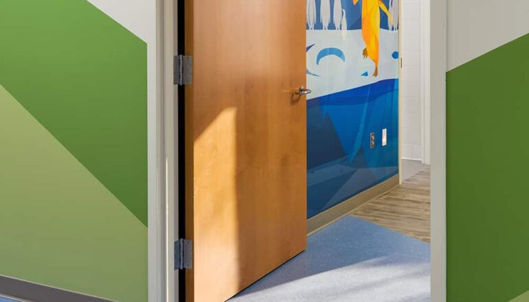 The door to a patient room with a view to a penguin wall mural.