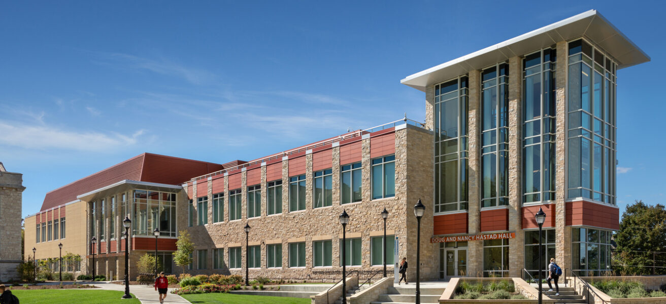 Students walk past the entry to Hastad Hall, a buff brick and terracotta roof building