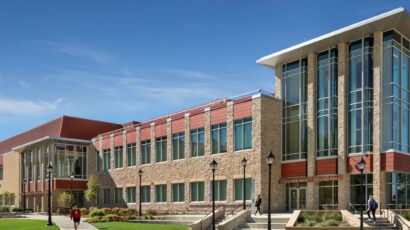 Students walk past the entry to Hastad Hall, a buff brick and terracotta roof building