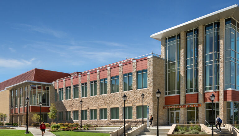 Students walk past the entry to Hastad Hall, a buff brick and terracotta roof building