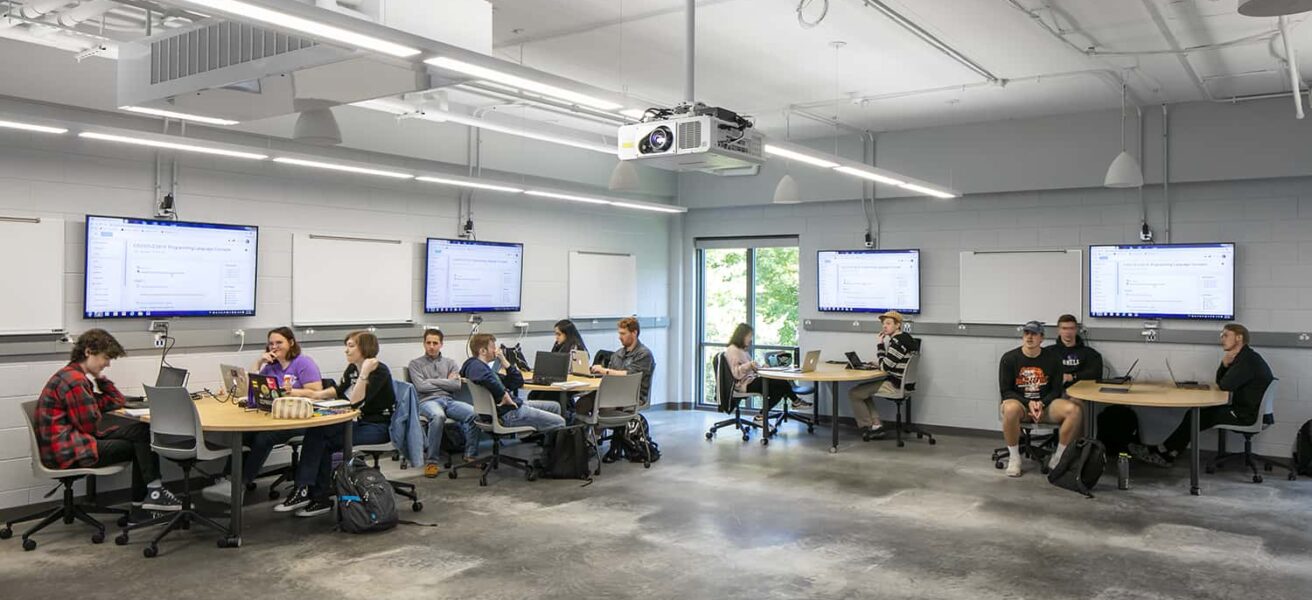 Students attending class in an active learning environment, complemented by mobile furniture, whiteboards, and large monitors.