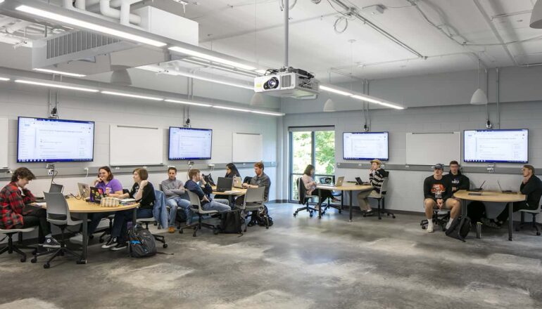 Students attending class in an active learning environment, complemented by mobile furniture, whiteboards, and large monitors.