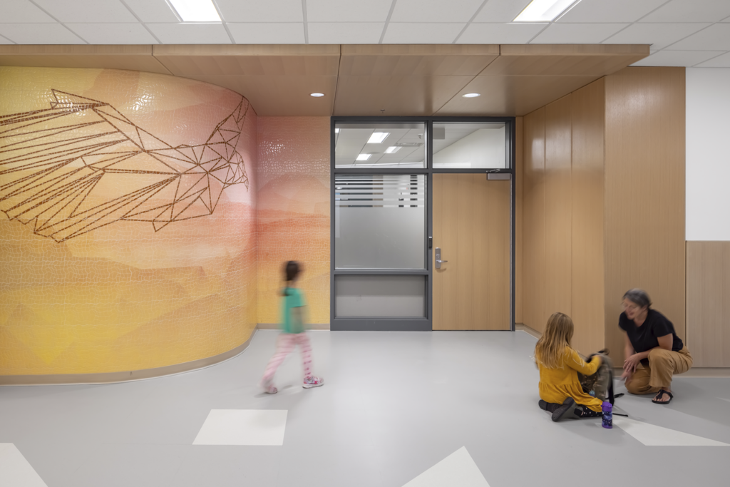 Students and a teacher walk toward a classroom entry that features an abstract hawk and sunset themed wall mural