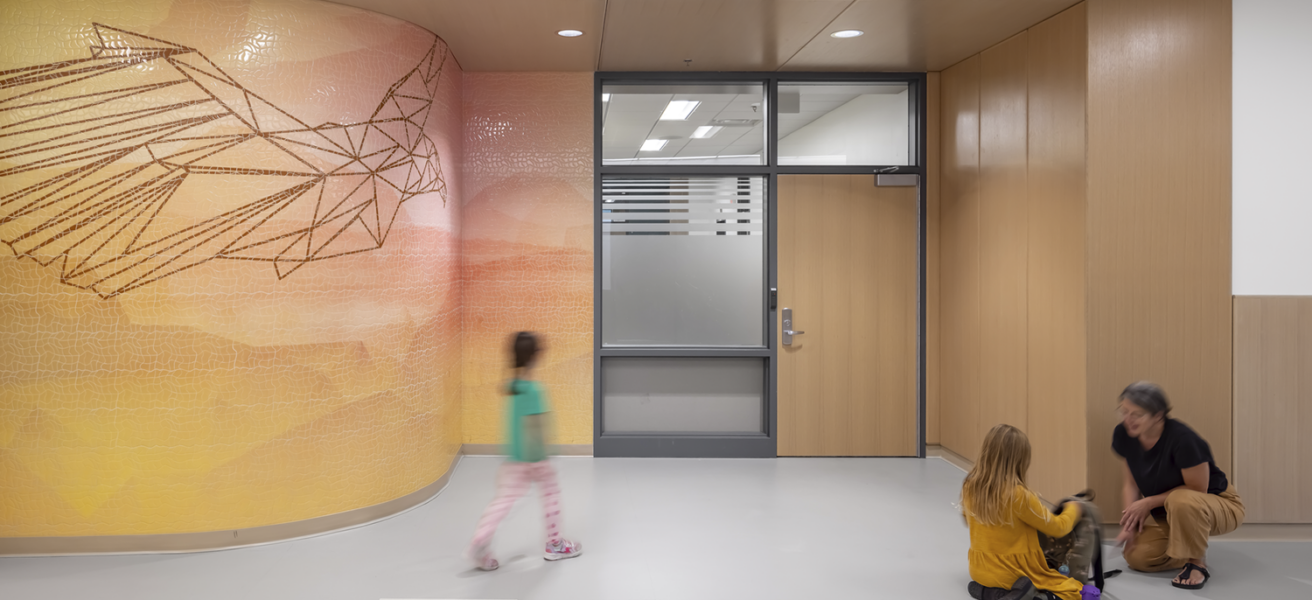 Students and a teacher walk toward a classroom entry that features an abstract hawk and sunset themed wall mural