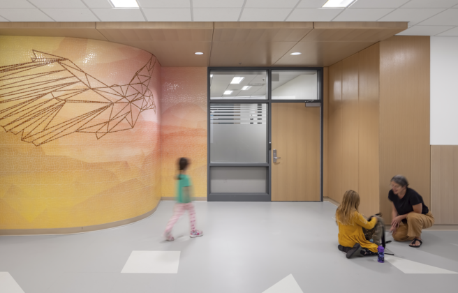 Students and a teacher walk toward a classroom entry that features an abstract hawk and sunset themed wall mural