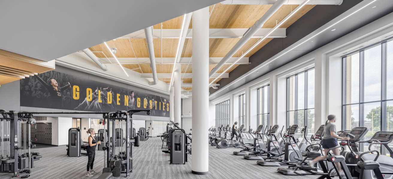 The main cardio area in the Lund Center features expansive views, high wood paneled ceilings, and branded wall graphics