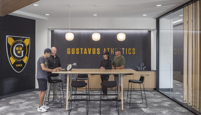 A student athlete prospect and their parents meet with a GAC coach in the recruiting room. A large Gustavus shield and branding enhance the experience