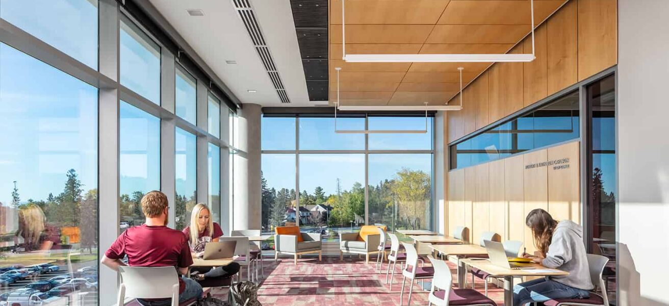 Students studying in a lounge space with floor to ceiling windows.