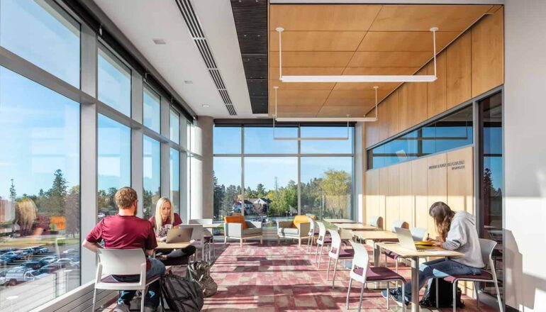 Students studying in a lounge space with floor to ceiling windows.