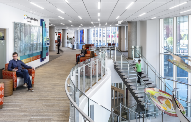 People utilize the public circulation spaces inside the Hennepin Healthcare Clinic & Specialty Center. Rainbow colored hanging artwork and a donor wall enhance the experience