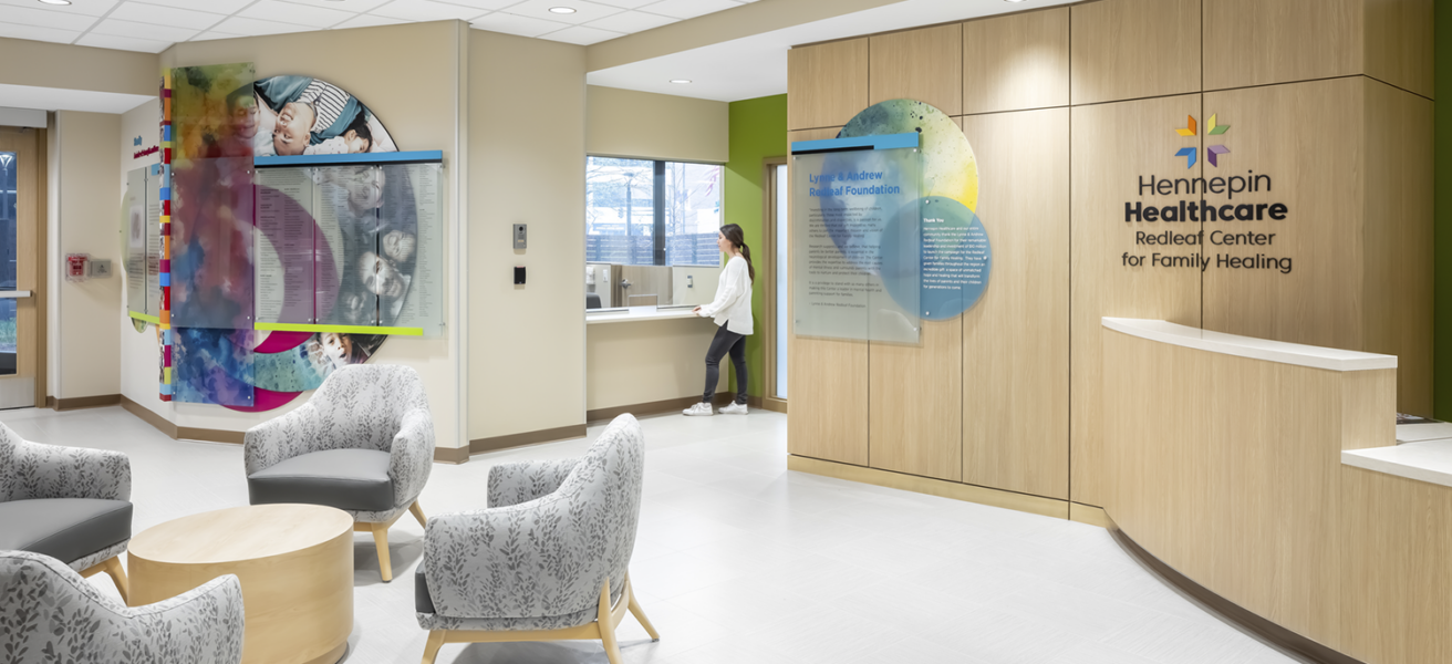 People talk at the Hennepin Healthcare Redleaf Center's reception desk, surrounded by colorful artwork and gray waiting chairs