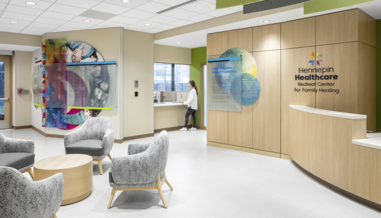 People talk at the Hennepin Healthcare Redleaf Center's reception desk, surrounded by colorful artwork and gray waiting chairs