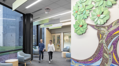 Two people enter the Redleaf Center and walk past a custom mosaic depicting a floor to ceiling tree