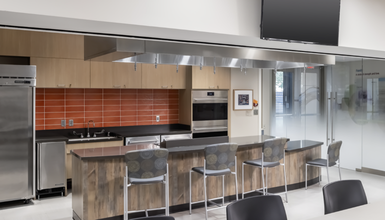 The Redleaf Center's kitchen has modern amenities, a large TV, dining space, and bartop chairs for teaching opportunities