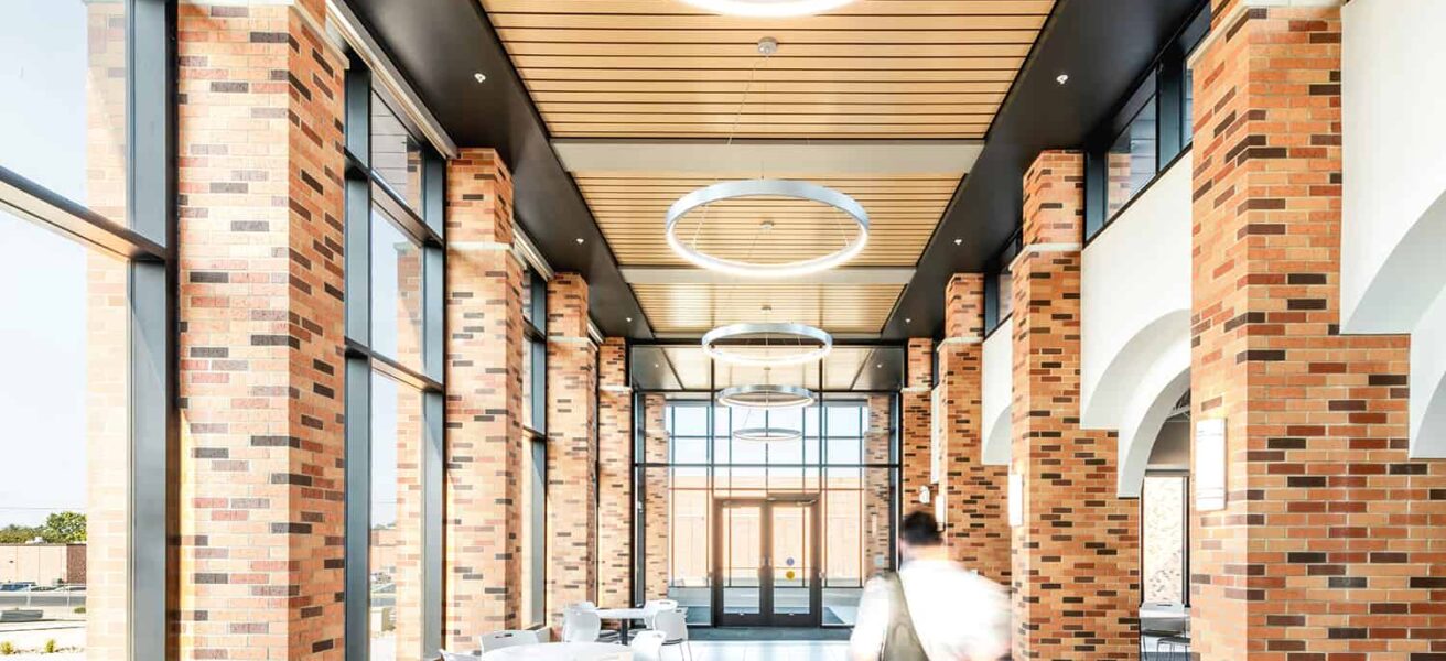 Interior corridor in the entry to the Healthcare Center of Learning, surrounded by exposed brick, wood paneling, feature circular lighting, and open seating.