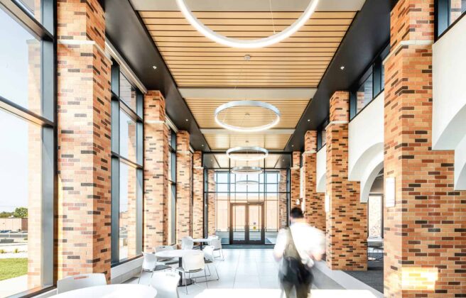 Interior corridor in the entry to the Healthcare Center of Learning, surrounded by exposed brick, wood paneling, feature circular lighting, and open seating.