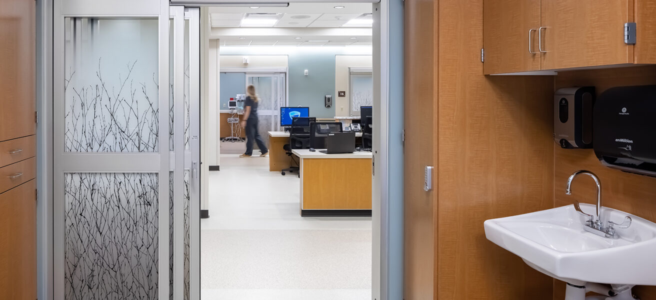 A view from inside a pre-post room into the corridor and nurse station in the MMC Ashland Surgery Center. Nature themed adhesive coats the sliding doors and gives privacy