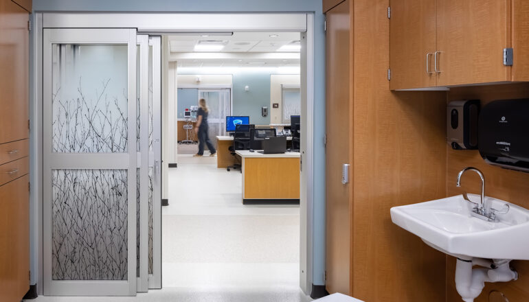 A view from inside a pre-post room into the corridor and nurse station in the MMC Ashland Surgery Center. Nature themed adhesive coats the sliding doors and gives privacy