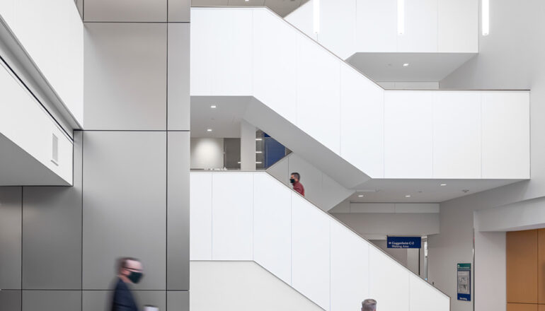 People walk through the Hilton Atrium and use the open grand staircase. Brightly colored blue, yellow, and gray furniture is available