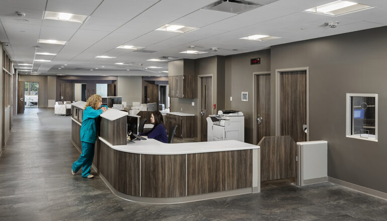 Two nurses hold a discussion at the wood-toned behavioral health unit nurse station