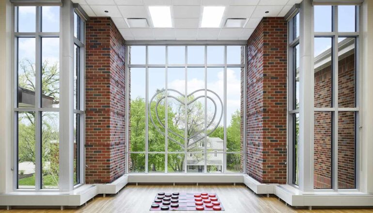 The children's indoor large motor room with toys and floor to ceiling windows that feature a heart accent.