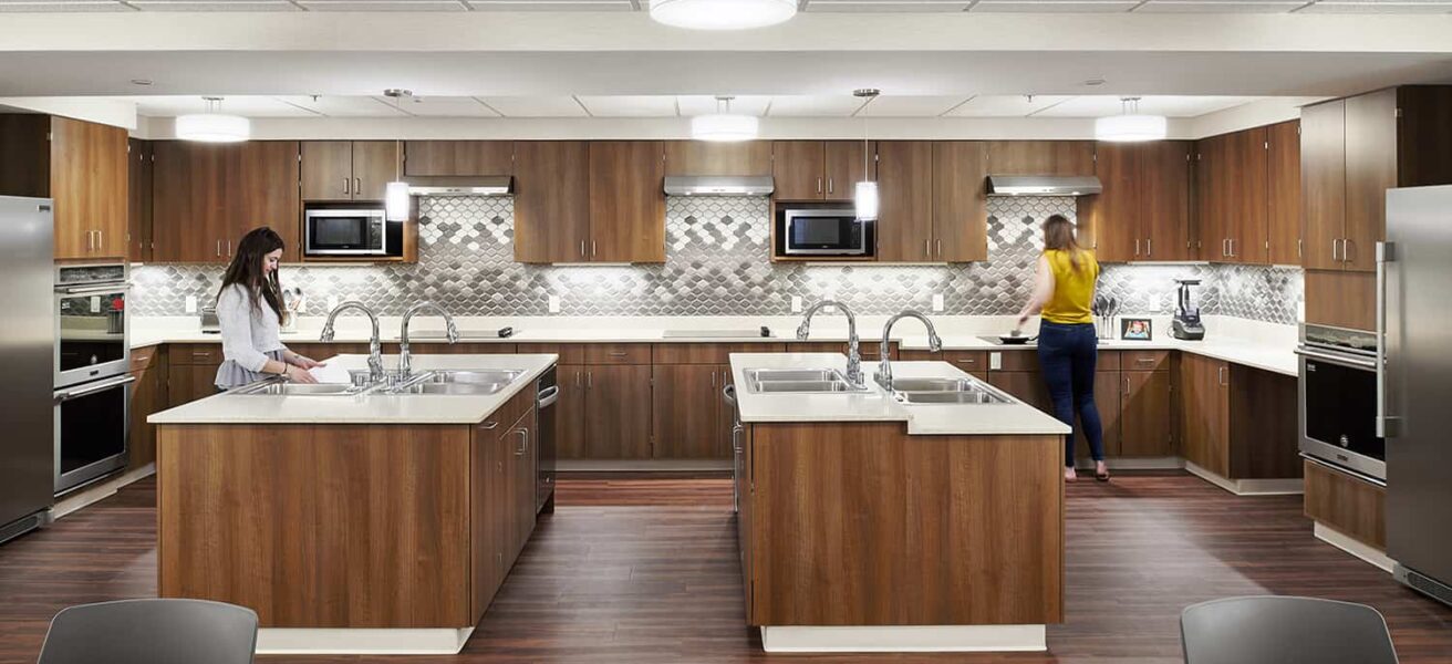 Focus on the shared kitchen area with four open food prep stations and warm wood paneling.