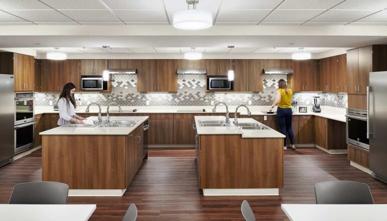 Focus on the shared kitchen area with four open food prep stations and warm wood paneling.