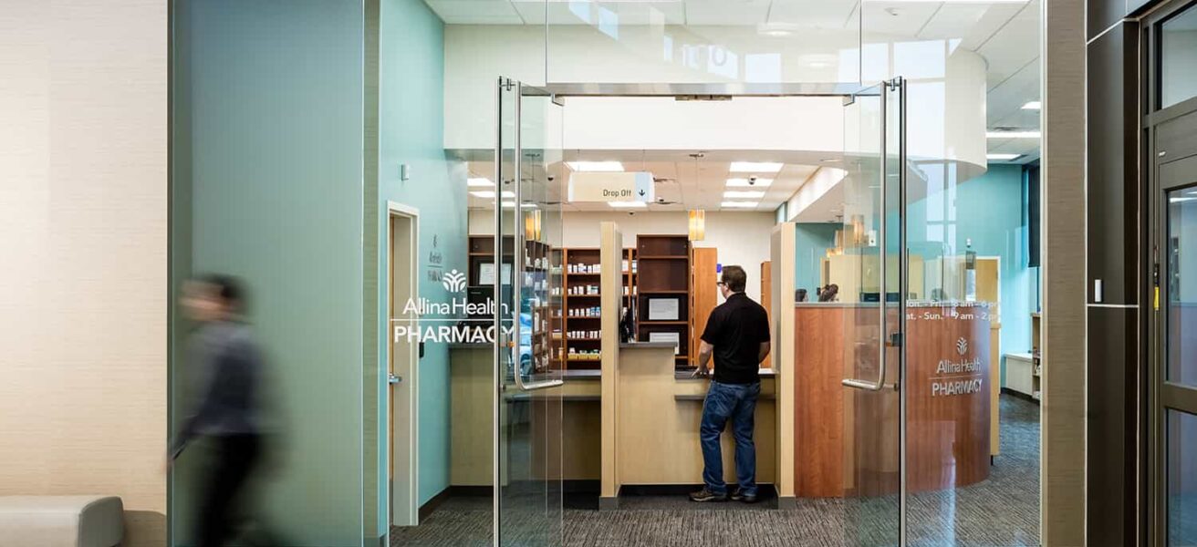 Entry to the Allina retail pharmacy with floor to ceiling glass and warm wood shelving.