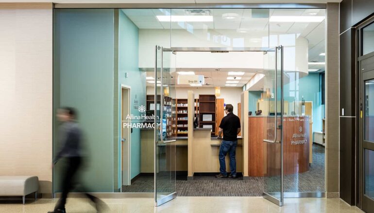 Entry to the Allina retail pharmacy with floor to ceiling glass and warm wood shelving.