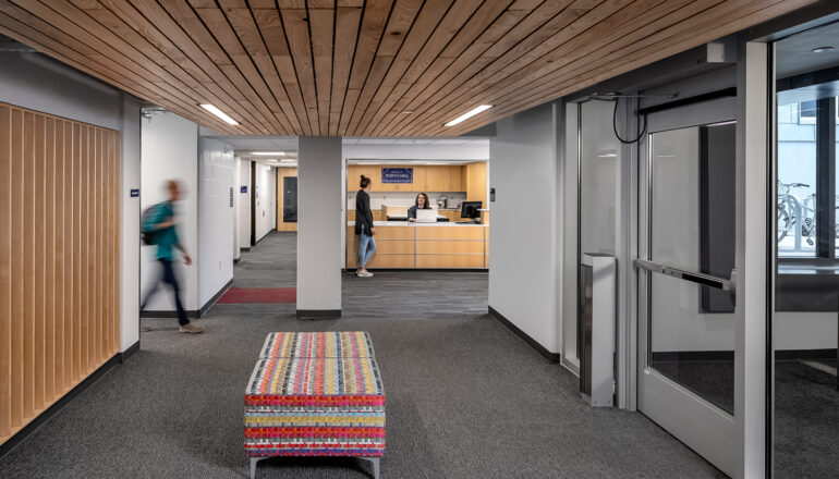 Students walk through North Residence Hall's lobby. A colorful bench and wood paneled ceiling welcome students to the color-coded residence hall