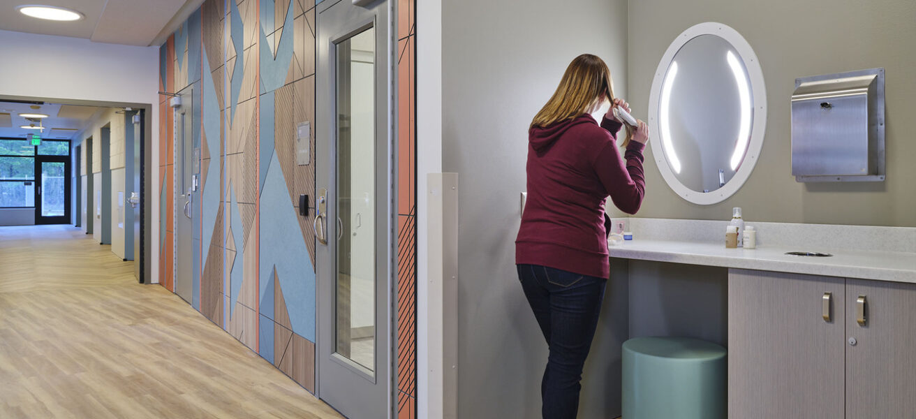 A person grooms themself in a Maple Lane patient corridor shared grooming station.