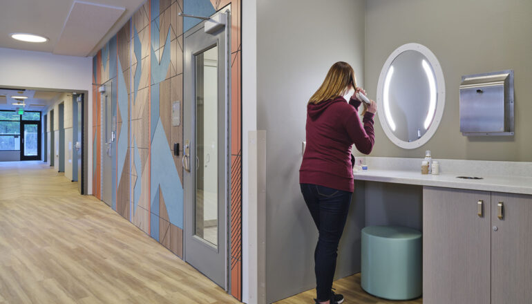A person grooms themself in a Maple Lane patient corridor shared grooming station.