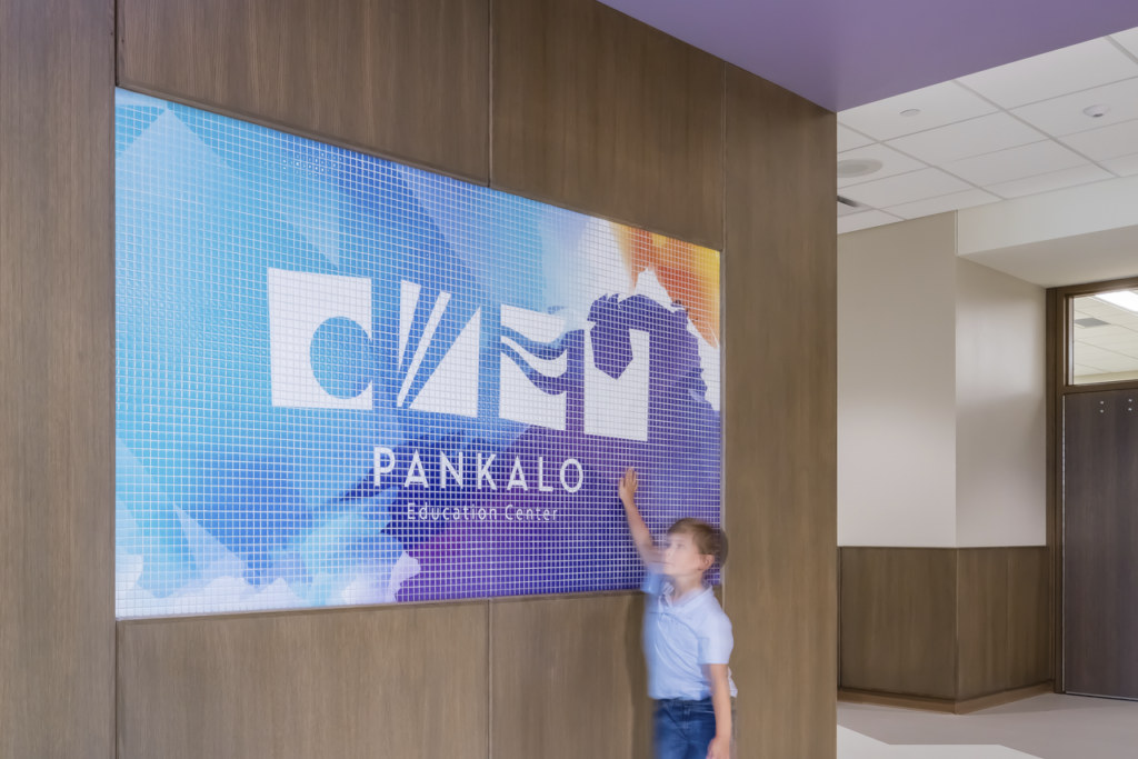A child walks past and touches the BWBR-designed Pankalo school logo.